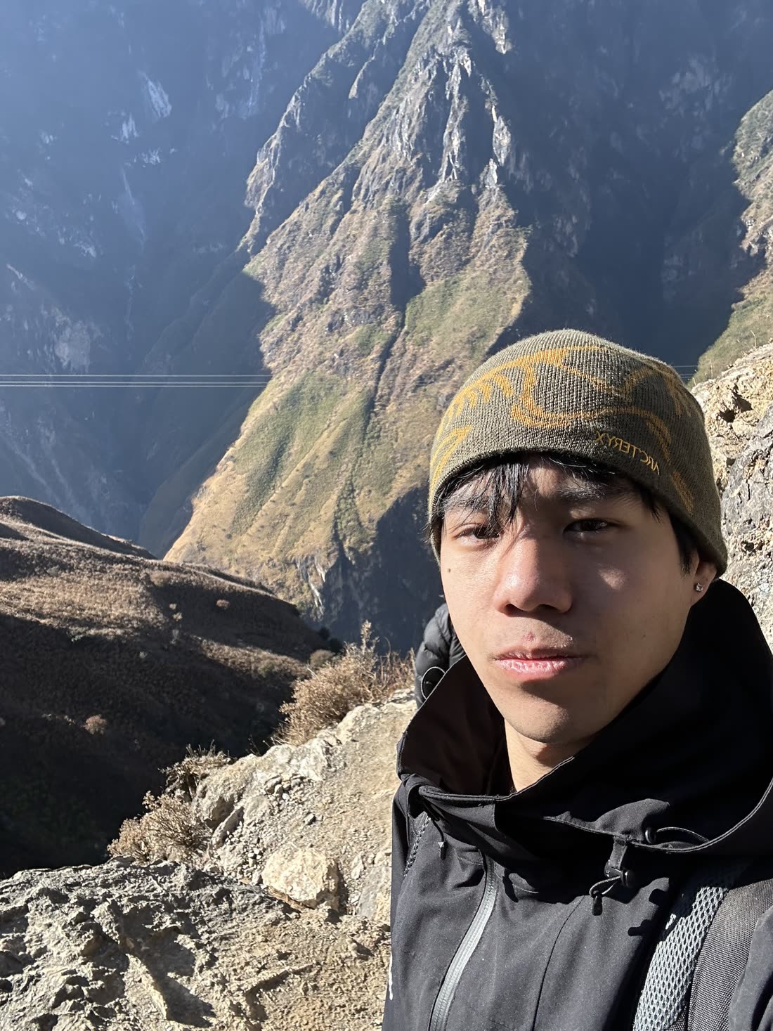 Standing on a ridge with a deep valley and snow-streaked mountain face behind.