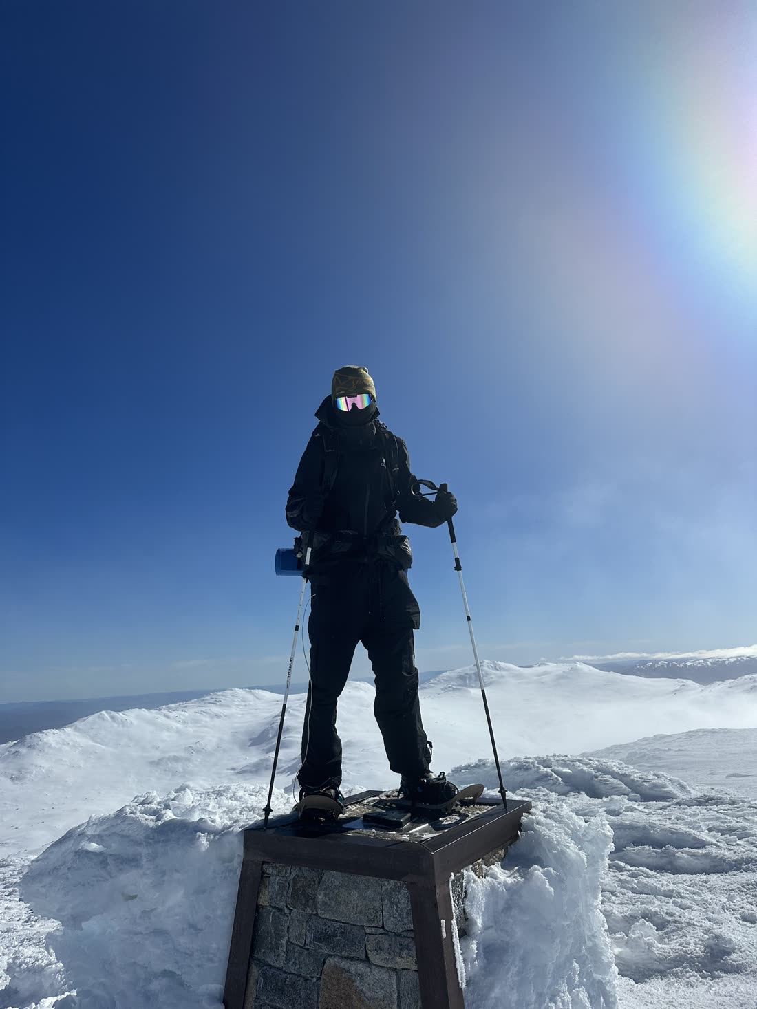 Standing on a summit trig point in snow, a sun halo arcing through the sky.